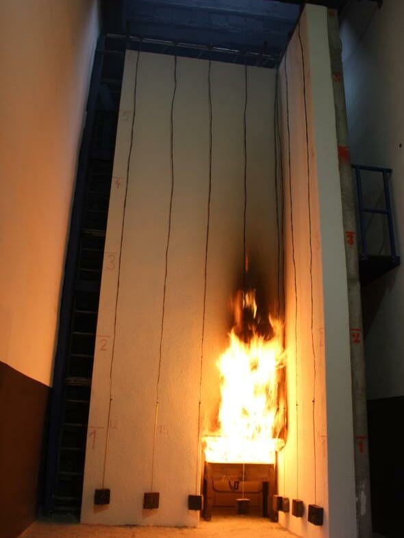 Fassadenbrandprüfstand während einer Brandprüfung mit einer in Flammen stehenden Fassade