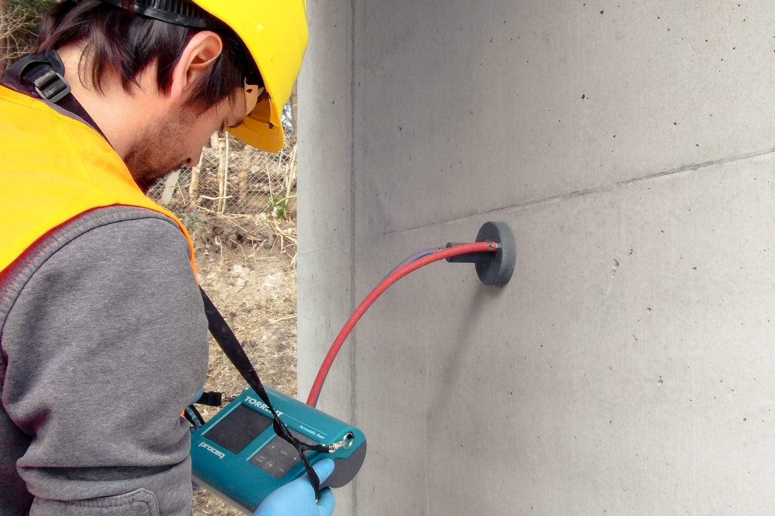 Gerät ( Torrent) zur Messung der Permeabilität von Beton an einer Betonstütze gehalten von einem Mann mit Bauhelm und Warnweste